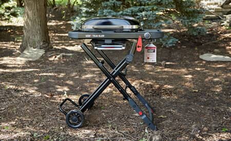 Weber Traveler folding gas grill beside a lake campsite